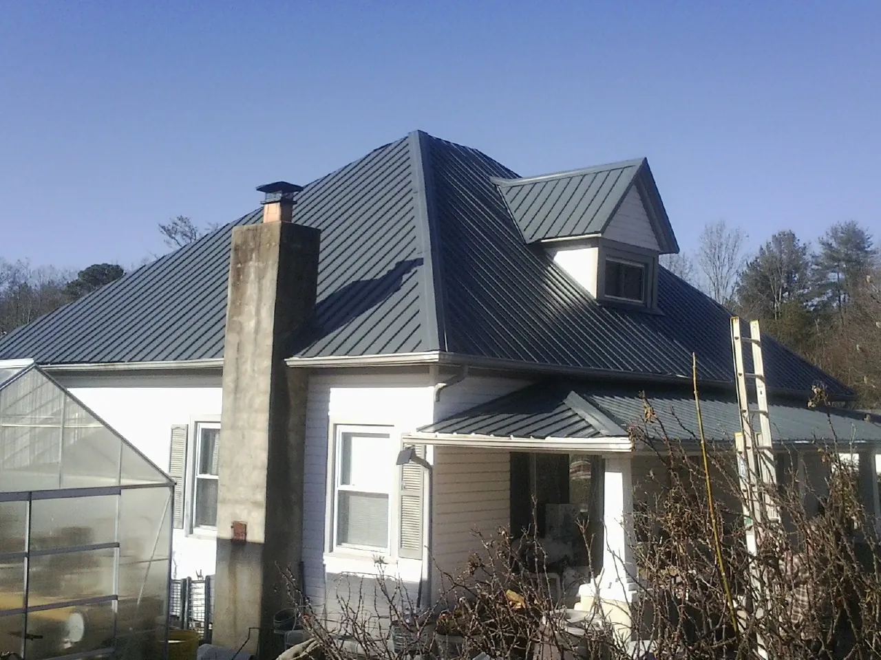 Dark blue standing seam metal roof on a white farmhouse with dormer — Slate & Tile Roof Repair by Roofing Brothers in Gilchrist