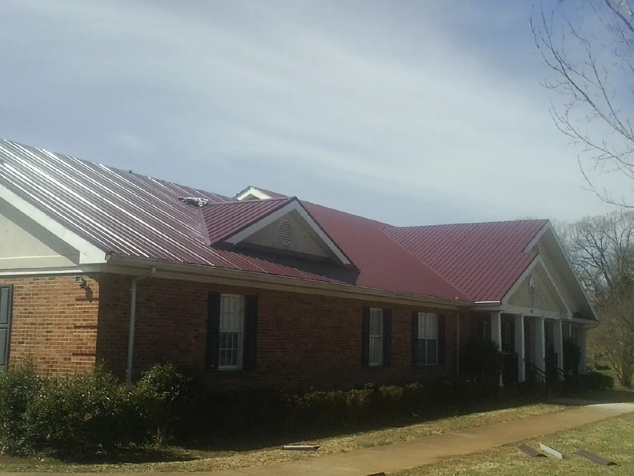 Red metal roof with gabled entries on a long brick building, from a Hail Damage Roof Repair job in Gilchrist