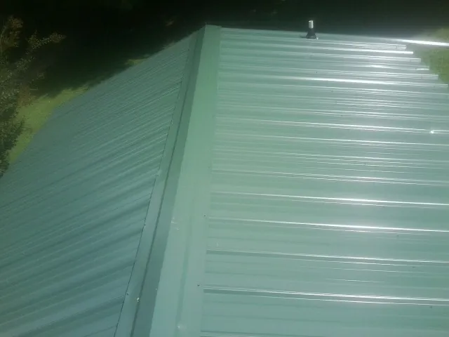 New green metal panels meeting at the ridge of a roof — Flat Roof Repair work by our crew in Gilchrist
