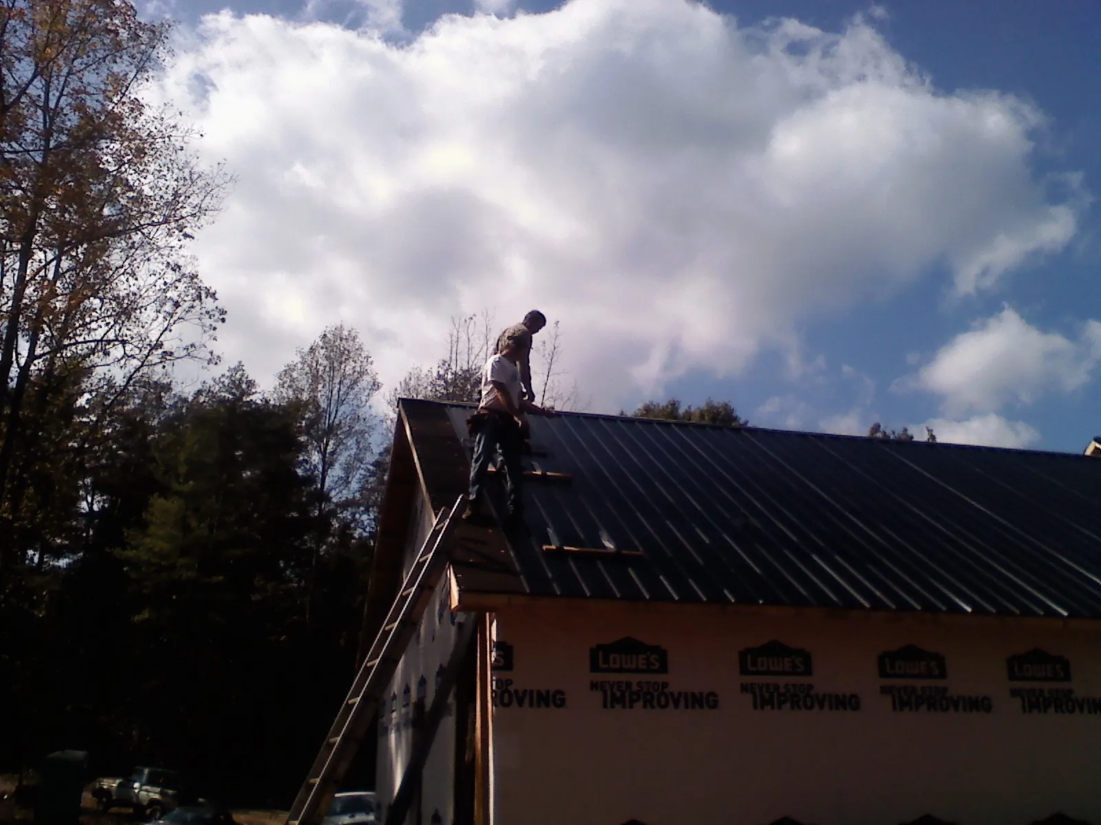 Roofer fastening dark metal panels high against a cloudy sky, from a Roof Inspection job in Gilchrist