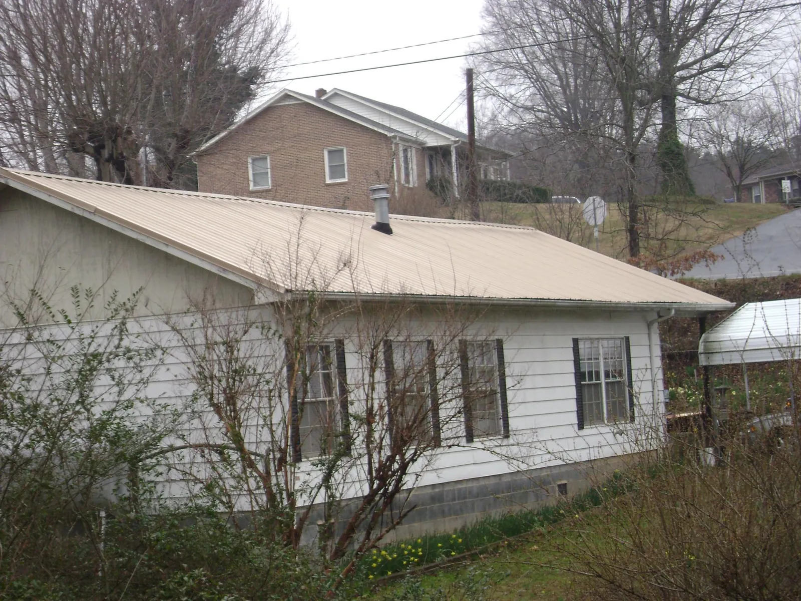 Tan metal roof on a white sided house set into a hillside — Commercial Roofing by Roofing Brothers in Gilchrist