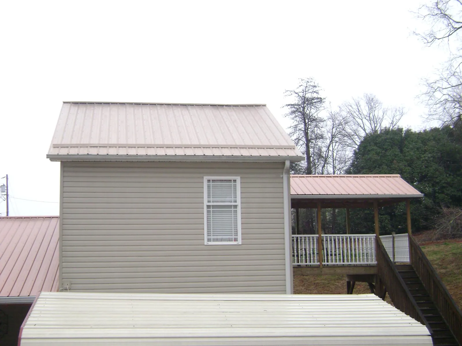 Tan metal roofs on a two story addition and attached porch, from a Roof Replacement job in Gilchrist