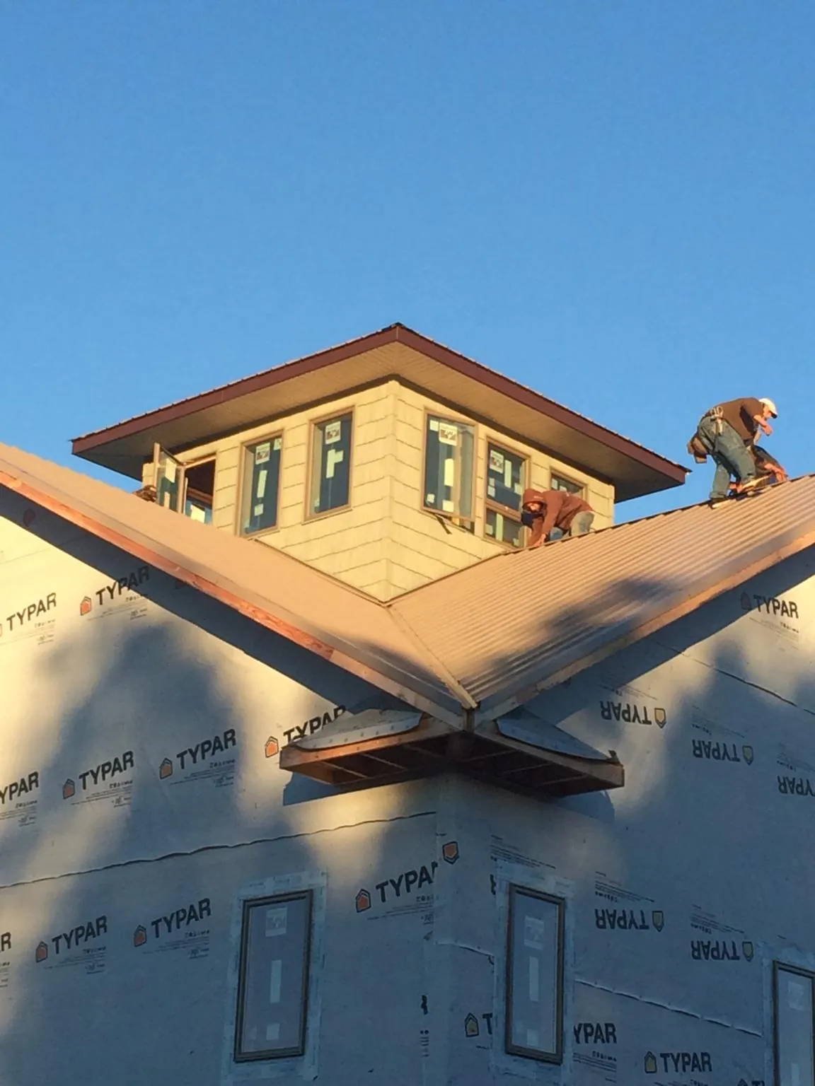 Roofers working around a rooftop cupola on a new metal roof at sunset — Roof Waterproofing in Gilchrist by Roofing Brothers